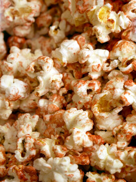 A close-up shot shows a pile of seasoned popcorn. The popcorn is white with reddish-brown seasoning sprinkled on it.
