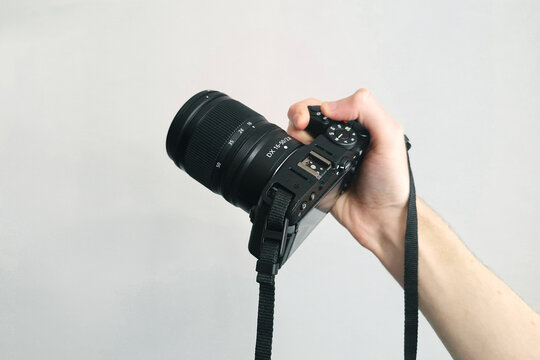 Professional photographer hand holds modern black camera with lens against clean background.