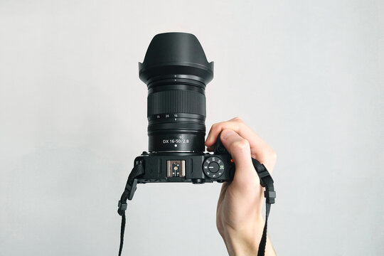 Human hand firmly holds professional camera with lens hood pointing forward on white background