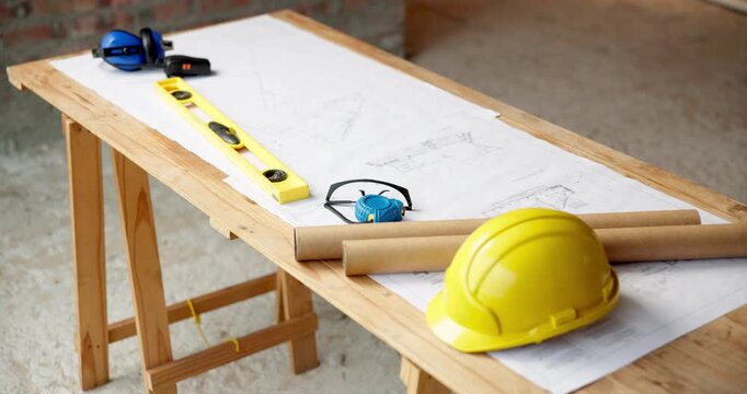 Architecture, hard hat and blueprint at empty site for building, maintenance or property development. Helmet, floor plan and equipment with PPE on desk by construction design for repair or renovation