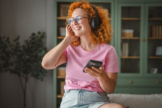Happy woman enjoying music at home using smartphone