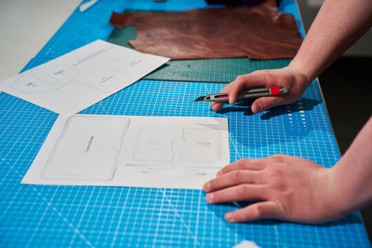 Artisan using a precision knife to cut a printed paper pattern on a blue cutting mat.