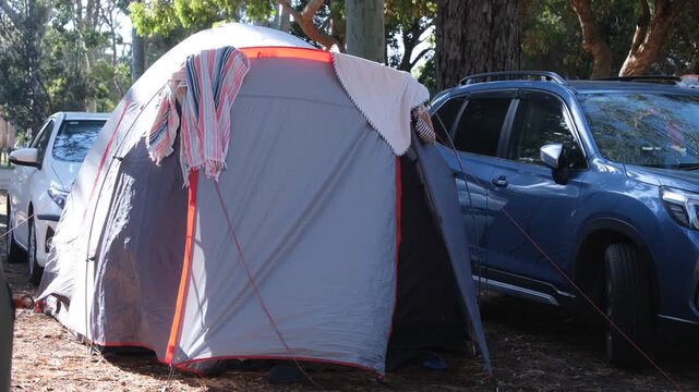 Family dome tent set up next to a parked SUV vehicle at a campground in Australia, beach towel hangs over the top to dry.  Roadtrip in the Australian outdoors.