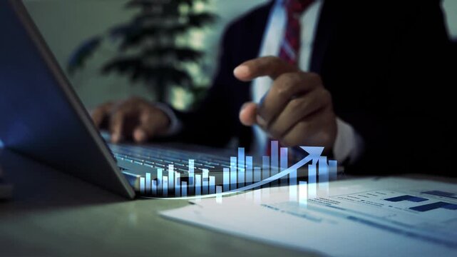 Businessman working on a laptop at a desk with papers and a glowing hologram bar chart on screen, Business data analysis finance planning 