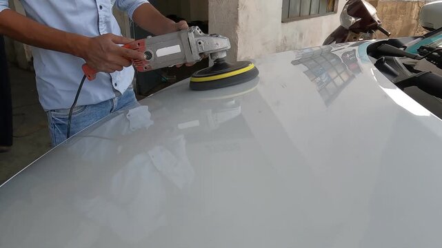 Professional detailer using a rotary machine buffer with a foam pad to polish the hood of a white car. The visual shows the smooth, shiny reflection on the car's surface as scratches are removed.