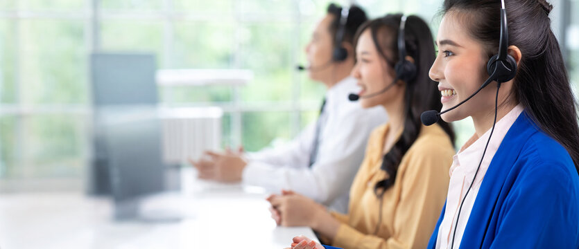 Asian woman operator and team working with headsets and desktop computer at telemarketing customer service