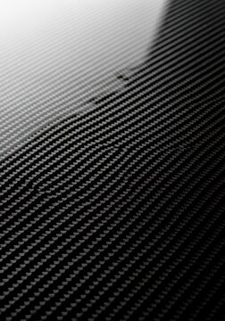 Close-up macro shot of a sleek black carbon fiber weave pattern with soft highlights reflecting off the glossy high-tech composite surface, light, shiny, fabric