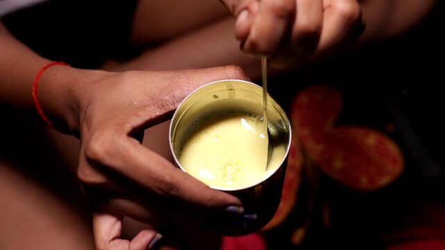 a women mixing turmeric milk in glass by her hand with the selected focus area 