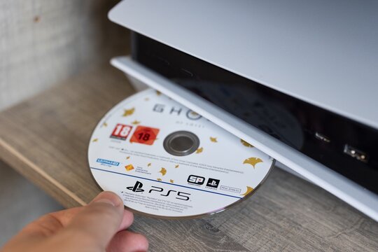 BRECHT, BELGIUM &ndash;July 10 2026: A close-up portrait of a hand putting a physical disk into the disk drive of a playstation 5 console, ready to play the game.