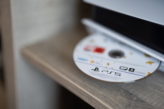 BRECHT, BELGIUM &ndash; July 10, 2026: Macro photo focusing on the interaction between a hand and a PlayStation 5 console while inserting a physical video game disc into the drive.