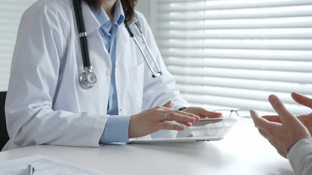 Doctor consulting patient, discussing medical information and diagnosis using a digital tablet during a healthcare visit at a modern clinic office
