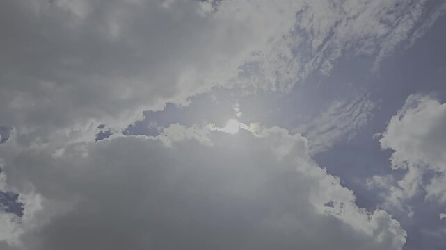 Large cumulus clouds fill the lower portion of the frame while bright sunlight breaks through gaps in the clouds, creating visible sun rays and a glowing halo effect.