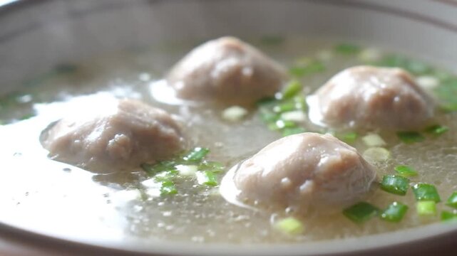 Savory meatball soup with fresh green onions served in a white bowl, a comforting homemade meal.
