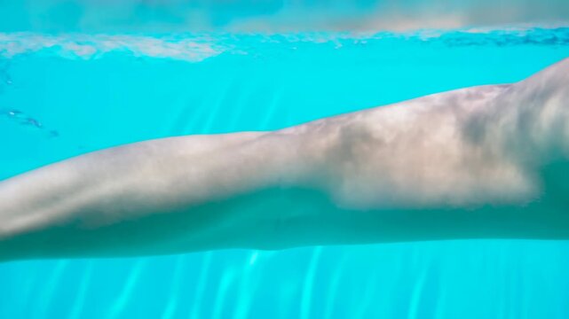 Underwater view of large marine mammal tail and fluke moving through shallow turquoise water with sunlit caustics, soft ripples, smooth skin, and tranquil ocean habitat