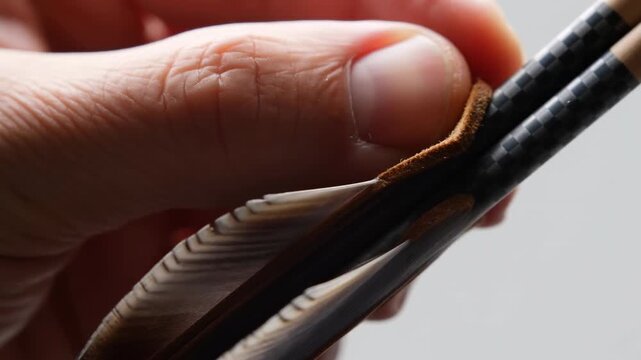 Thumb and index finger pinching patterned shafts with fletchings and suede tabs in tight macro close-up conveying hands-on inspection