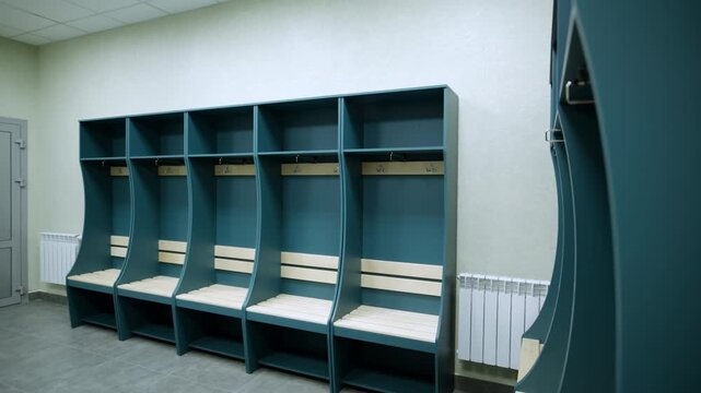 Rows of modern curved teal open lockers line minimalist dressing room. Integrated light wooden benches provide comfortable seating below