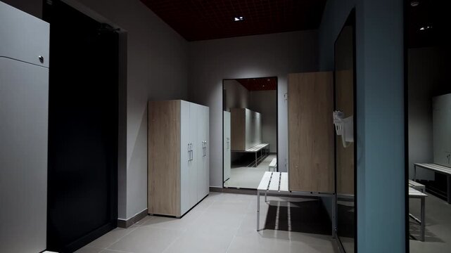 Lockers arranged under dramatic grid ceiling with large floor-to-ceiling mirror. Integrated wooden benches emphasize modern facility design