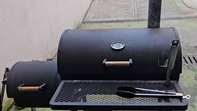 Black Offset Smoker Grill With Thermometer and Barbecue Tongs Smoking During Outdoor Cooking Preparation