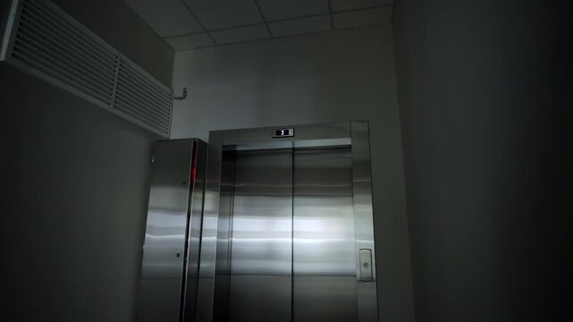 Sleek metal elevator doors stand centered in dimly lit corner hallway. Digital indicator displays floor number. Modern design of interior