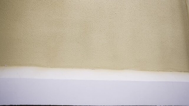 Smooth camera movement across a beige stucco wall with white baseboard and red pipes below.