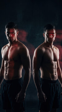 Dual Strength: Two muscular men with sculpted physiques stand side by side, their powerful bodies illuminated by dramatic red lighting against a dark, smoky background.
