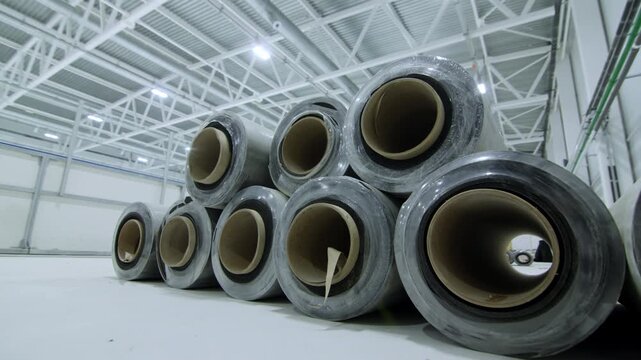 Warehouse stores large material rolls wrapped in protective plastic film. Storage system provides efficient resource management in facility