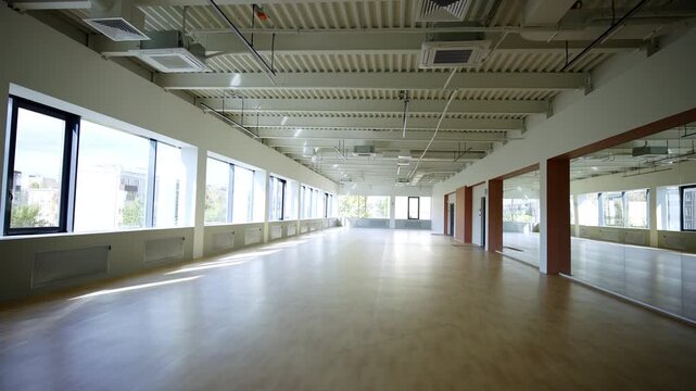 Empty indoor sports hall with wooden floor and exposed metal structure ceiling. Large windows line wall providing natural daylight