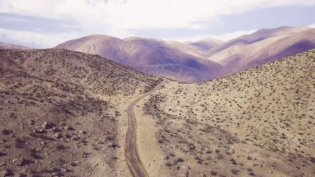 Aerial namibia mauve hills meeting valley with faint snaking track, soft pastel ridgelines, dusted texture and cool shadow layers under late afternoon light