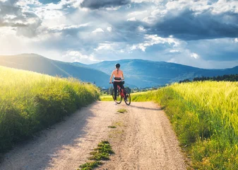 Female cyclist with mountain bike standing on dirt road in Slovenia countryside in summer. Woman looking at beautiful valley and mountains under dramatic stormy sky. Summer outdoor activity © den-belitsky