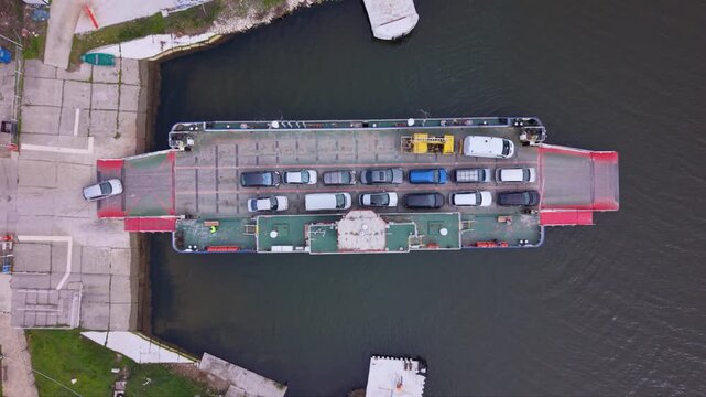 Aerial drone view of vehicle ferry transporting cars across a wide river with automobiles boarding and disembarking at ferry terminal connecting opposite riverbanks transportation infrastructure RO-RO