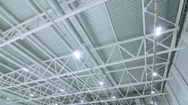 High ceiling structure includes air ducts cables and lighting fixtures. Engineered layout demonstrates high functionality of modern plant