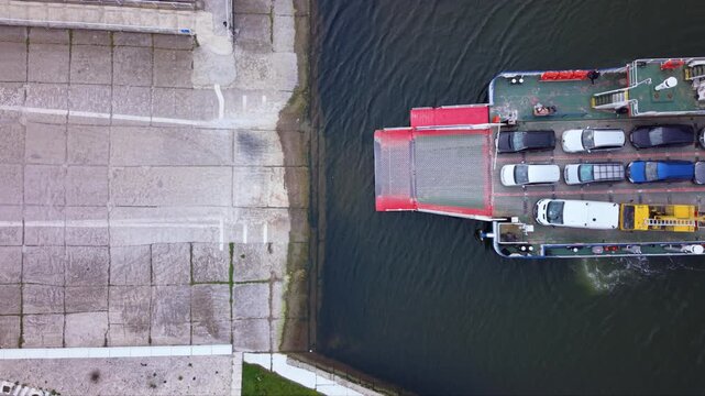 Aerial drone view of vehicle ferry transporting cars across a wide river with automobiles boarding and disembarking at ferry terminal connecting opposite riverbanks transportation infrastructure RO-RO