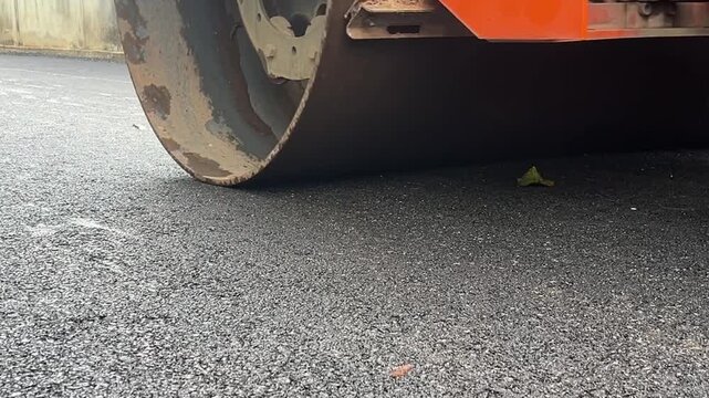 Road Roller Compacting Asphalt: A close-up view of a road roller's drum pressing down on a freshly paved asphalt surface, smoothing and compacting the material for a durable road.