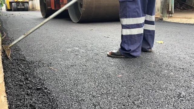 Road Construction: A road worker in reflective uniform operates a steamroller to compact freshly laid asphalt, essential for building and maintaining modern infrastructure.
