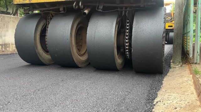 Road Roller Compacting New Asphalt: Heavy-duty road roller with multiple wide tires compresses freshly laid asphalt on a street, showcasing the infrastructure construction process.
