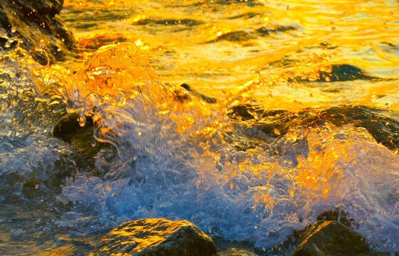 Dynamic golden water splash with waves crushing stones in golden sunset, water splash background