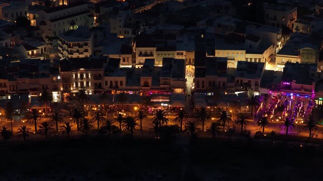 Aerial drone view of the seafront promenade at night, illuminated tavernas and bars below the old town, Rethymno, Greece