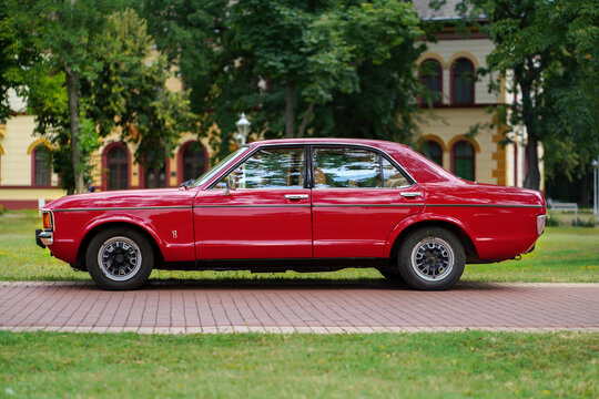 Ford Granada (Ford Consul) Mk1 Classic Sedan - side profile view of a vintage red 1970s sedan automobile parked on a brick path near green trees in Palic, Serbia on July 5, 2026.