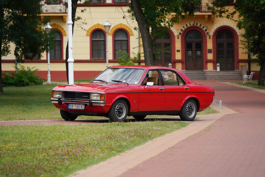 Ford Granada (Ford Consul) Mk1 Classic Sedan - front angle view of a vintage red retro automobile driving on a park walkway near a historic hotel building in Palic, Serbia on July 5, 2026.