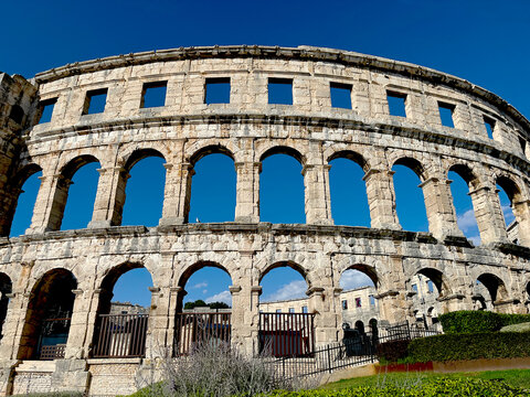 Ancient Roman amphitheater Pula Arena surrounded by green bushes under blue sky