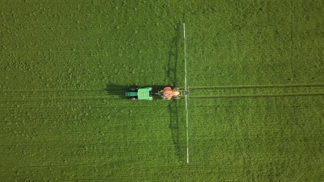 Aerial view of agricultural spraying on a lush green field, with a tractor pulling a wide boom sprayer across crop rows