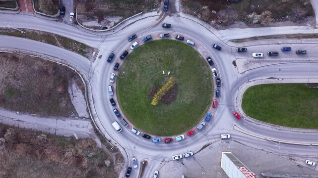Aerial top down drone view of busy urban roundabout with circulating traffic and multiple cars navigating circular intersection showcasing city road infrastructure transportation network and traffic f