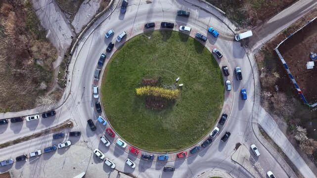 Aerial top down drone view of busy urban roundabout with circulating traffic and multiple cars navigating circular intersection showcasing city road infrastructure transportation network and traffic f