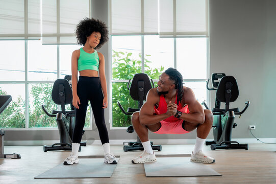 Black fitness coach dad showing squat exercise afro hair girl. Scene for family wellness, personal trainer mentoring child, bodyweight workout and health communication.