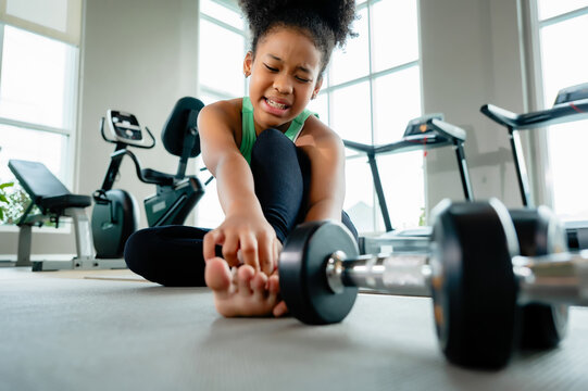 African American girl feeling pain foot ankle injury gym workout. Concept of sports injury, accident during exercise, first aid needed and physical pain.