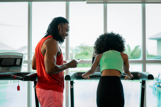 Back view afro hair teen girl training treadmill with supportive father. Concept of supportive family, healthy lifestyle habits, teenager health care and sport education.
