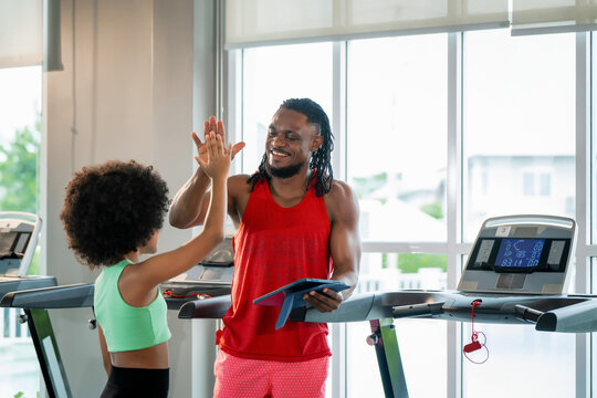 Black fitness coach dad smiling giving high five afro hair girl. Scene for personal coaching success, cardio endurance achievement, workout tracking and happy parenting.