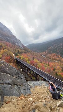 Oct 14, 2021 - Crawford, New Hampshire. Notch Train Passes Timelapse. New Autumn Fall Foliage Colors Photo Couple Pose on Rocks. (Vertical Video)
