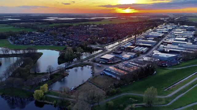 Aerial wide angle panoramic view over an industrial commercial zone and a residential town neighborhood alongside historic star fortress water moats under a bright golden sunset sky