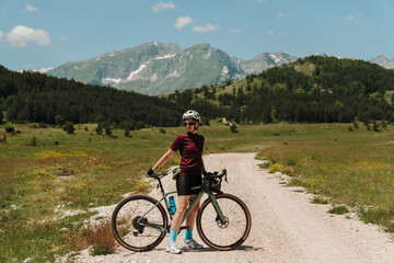 Fototapeta premium Woman posing on a gravel bicycle in Durmitor National Park, Montenegro. Summer bikepacking journey surrounded by alpine mountain landscapes.